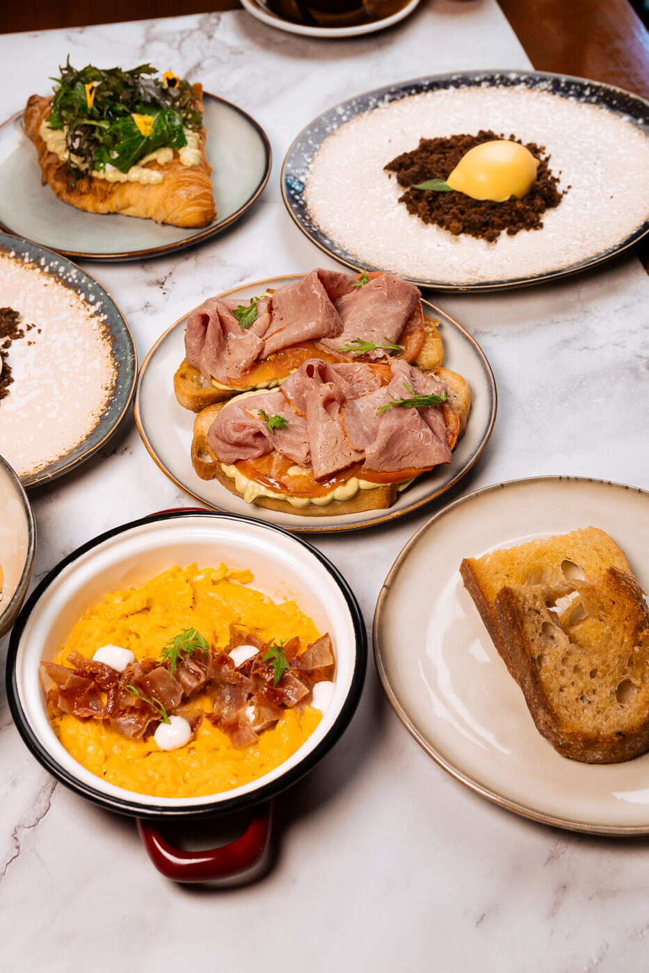 Mesa de brunch completa en Santolia: huevos revueltos con jamón serrano, croissant y tostadas